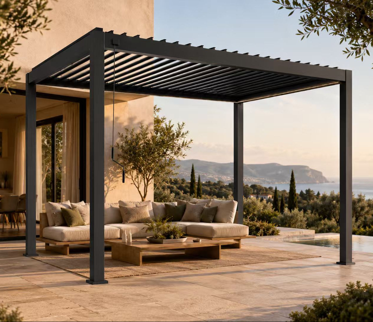 A modern black metal pergola with a slatted roof over a patio seating area, featuring a beige outdoor sofa, wooden coffee table, and a scenic coastal view in the background.